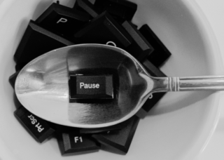 Grafika przedstawiająca białą miskę, w której znajdują się czarne klawisze klawiaturowe, w tym przycisk pause leżący na łyżce.