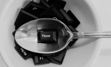 Grafika przedstawiająca białą miskę, w której znajdują się czarne klawisze klawiaturowe, w tym przycisk pause leżący na łyżce.