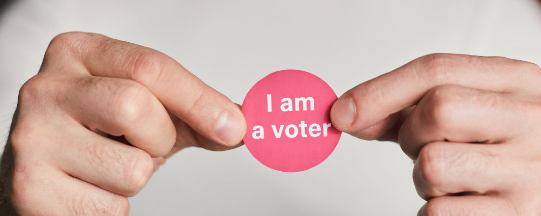Zbliżenie na dłonie trzymające naklejkę z angielskim napisem „I am a voter" co w tłumaczeniu oznacza „Jestem wyborcą".